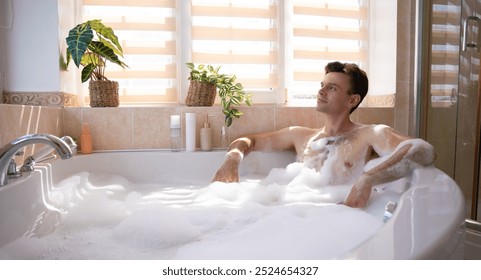 Handsome man enjoys a relaxing bubble bath in a sunlit bathroom. He leans back contentedly, surrounded by plants and bath products, conveying a sense of calm and self-care in a modern, cozy setting - Powered by Shutterstock