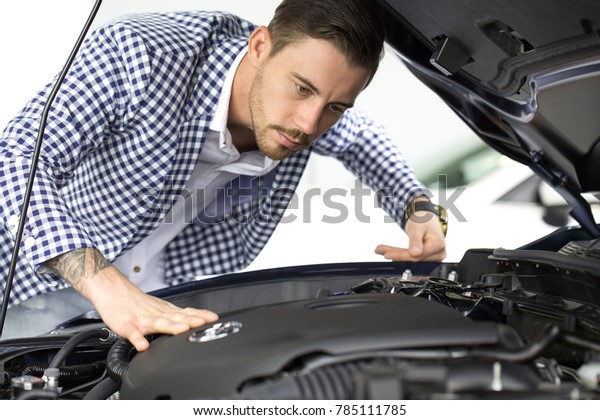 Handsome man examining engine of a car while\
choosing a new auto at the dealership transportation vehicle\
technology modern machinery horsepower drive travel automotive\
lifestyle retail\
rental.
