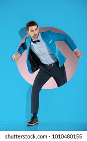 Handsome Man In Fashionable Clothes Stepping Through Aperture On Blue