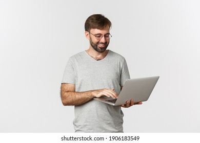 Handsome Man Freelancer, Working With Laptop And Smiling, Wearing Glasses And T-shirt, Standing Over White Background