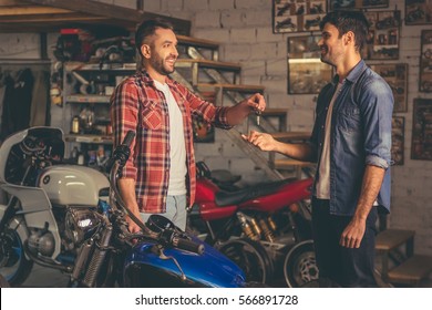 Handsome Man Is Giving A Key To The Owner Of The Motorcycle While Both Are Standing In The Repair Shop