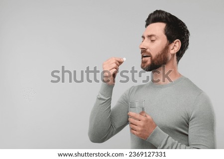 Handsome man with glass of water taking pill on light grey background, space for text
