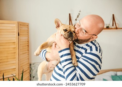 Handsome man with glasses cradling a small French Bulldog in his arms. - Powered by Shutterstock