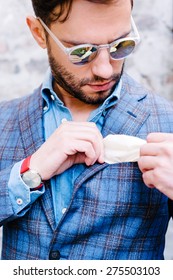 Handsome Man With Glasses In A Suit, Against Old Vintage Wall, Fixing His Pocket Square