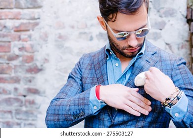 Handsome Man With Glasses In A Suit, Against Old Vintage Wall, Fixing His Pocket Square