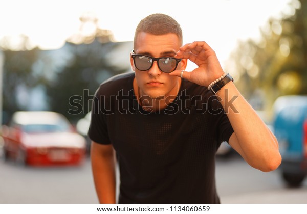 handsome man with a hairstyle in sunglasses and a\
black fashion t-shirt at\
sunset