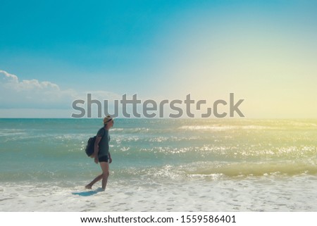 A handsome man in a hat and with a backpack walks barefoot along the edge of the sea on a hot sunny day. Travel concept. Vacation concept.