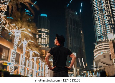 handsome man in hat fashionable clothes, brutal man, stylish outfit, walk down the street. cool light and palms in night city. Dubai