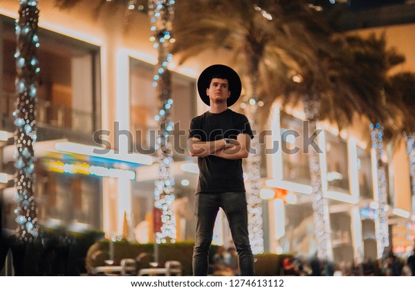 handsome man in hat fashionable clothes, brutal\
man, stylish outfit, walk down the street. cool light and palms in\
night city. Dubai