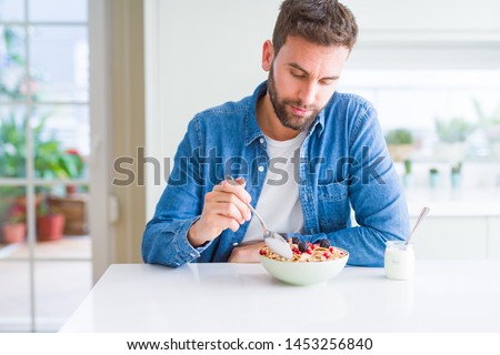 Handsome man having breakfast eating cereals at home and smiling