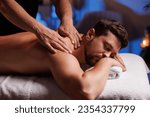 Handsome man having restorative back massage in spa salon, enjoying relaxing atmosphere, recharging after work. Masseuse gives therapeutic back massage to a visitor, the concept of healthy lifestyle.