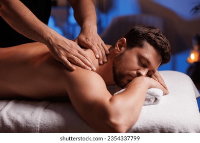 Handsome man having restorative back massage in spa salon, enjoying relaxing atmosphere, recharging after work. Masseuse gives therapeutic back massage to a visitor, the concept of healthy lifestyle. - Shutterstock ID 2354337799