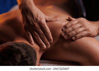 Handsome man having restorative shoulder massage in spa, enjoying relaxing atmosphere, rebooting after work. Masseuse performs therapeutic massage of the injured hand of visitor, restoring health. - Powered by Shutterstock