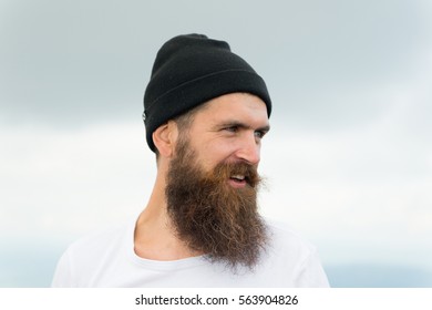 Handsome man hipster or guy with beard and moustache on smiling happy face in hat outdoor with cloudy sky on natural background