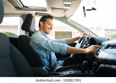 Handsome Man In His 30s Sitting In The Driver's Seat And Smiling. Taxi Driver Listening To Music On The Car And Changing The Radio Station