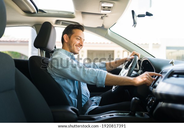 Handsome man in his 30s sitting in the driver\'s\
seat and smiling. Taxi driver listening to music on the car and\
changing the radio\
station