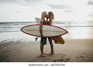 Handsome man and his girlfriend are kissing against background of sea and holding surfboards - Powered by Shutterstock