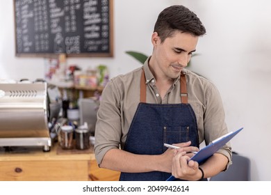 Handsome Man Holding Blue Folders In A Cafe, He Is Preparing To Open A Shop To Serve Customers, A Male Employee Opens A Shop To Serve Food And Drinks. Food And Beverage Service Concept.