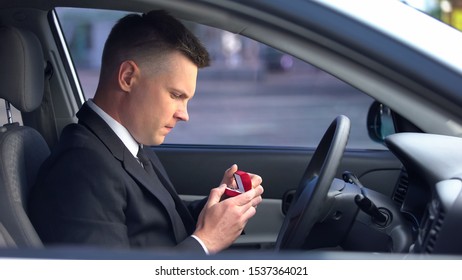 Handsome Man Holding Box With Engagement Ring Sitting In Car, Feeling Unsure