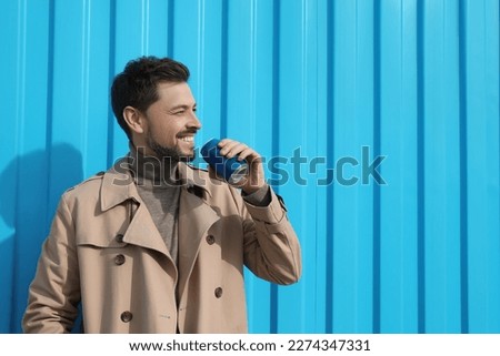 Handsome man holding tin can with beverage near light blue wall. Space for text
