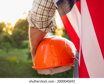 Handsome man holding US Flag against the background of trees, blue sky and sunset. View from the back. Labor and employment concept - Shutterstock ID 2000040692