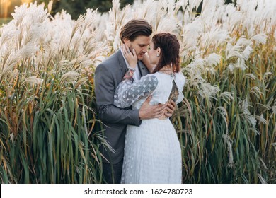 Handsome Man Hugging Beautiful Pregnant Woman In White Dress At Uruguayan Pampas Grass Background In Evening 