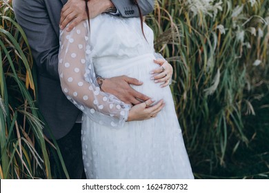 Handsome Man Hugging Beautiful Pregnant Woman In White Dress At Uruguayan Pampas Grass Background In Evening 