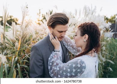 Handsome Man Hugging Beautiful Pregnant Woman In White Dress At Uruguayan Pampas Grass Background In Evening 