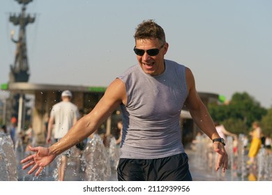 Handsome Man Jogging Among Dry Fountains In The Hot Summer Day In The Big City. Time To Cold. Fresh Water Splashes. Concept Of The Leisure Time, Freshness And Happiness. Frontal View