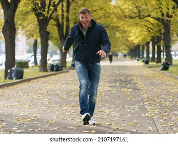 Handsome Man Jogging In Street In Autumn Day In The Big City Moscow. Time To Warm. Concept Of The Leisure Time, Good Mood And Sport Activity. Frontal View. 