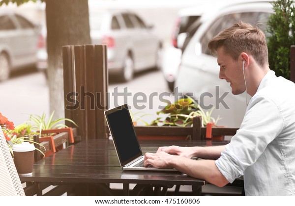 Handsome man with\
laptop listening music in\
cafe