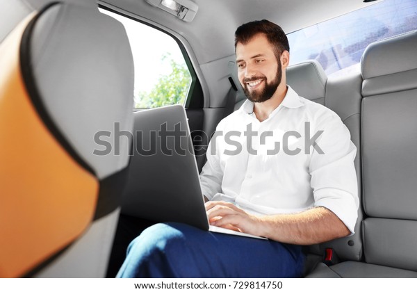 Handsome man with\
laptop on backseat of\
car