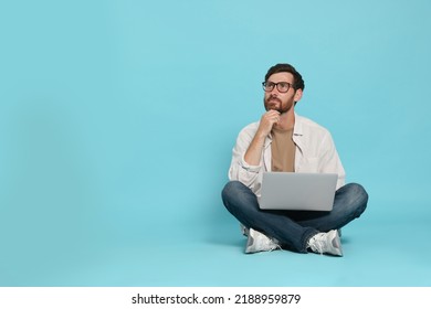 Handsome man with laptop sitting on light blue background