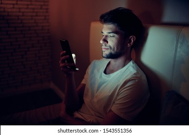 A handsome man lies in bed at night looking at the phone