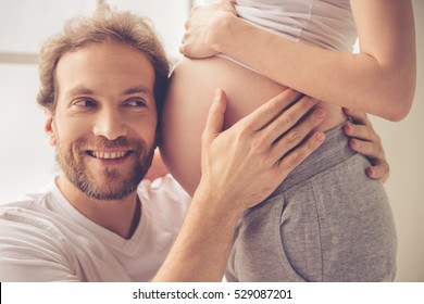 Handsome man is listening to his beautiful pregnant wife's tummy and smiling