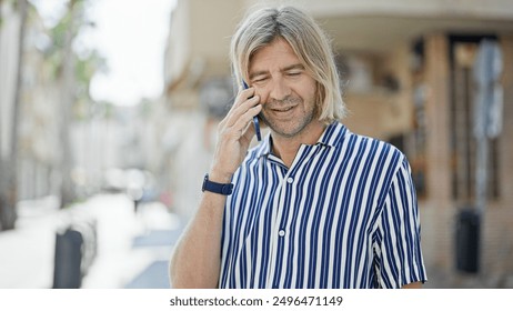 Handsome man with long blond hair talking on phone in sunlit urban street - Powered by Shutterstock