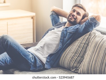 Handsome man is looking away and smiling while sitting on couch at home
