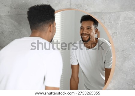 Handsome man looking at himself in mirror at home