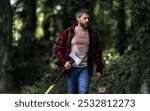 Handsome man or lumberjack in checkered shirt hold axe. Lumberjack or woodman. Masculinity concept. Man brutal strong attractive guy cutting wood with axe in forest. Lumberjack with big axe in forest.