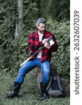 Handsome man or lumberjack in checkered shirt hold axe. Lumberjack or woodman. Masculinity concept. Man brutal strong attractive guy cutting wood with axe in forest. Lumberjack with big axe in forest.