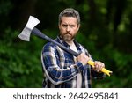Handsome man or lumberjack in checkered shirt hold axe. Lumberjack or woodman. Masculinity concept. Man brutal strong attractive guy cutting wood with axe in forest. Lumberjack with big axe in forest.