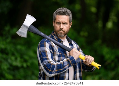 Handsome man or lumberjack in checkered shirt hold axe. Lumberjack or woodman. Masculinity concept. Man brutal strong attractive guy cutting wood with axe in forest. Lumberjack with big axe in forest.