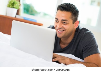 Handsome man lying in bed and watching something on laptop - Shutterstock ID 266080016