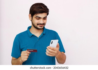Handsome Man Makes A Payment, Using A Credit Card And Smartphone. Photo Of Indian Man In T-shirt On Isolated Background.