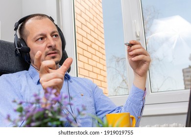 Handsome man makes a podcast audio recording at home iat window. smiling radio host in headphones recording podcast in broadcasting studio. attractive man with headphones and laptop talking on mic.