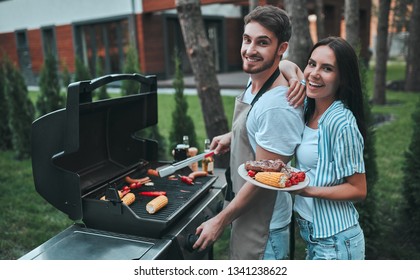 Handsome man is making grill barbecue. Group of friends are having bbq party outdoors on the backyard.