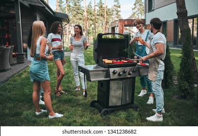 Handsome Man Is Making Grill Barbecue. Group Of Friends Are Having Bbq Party Outdoors On The Backyard.