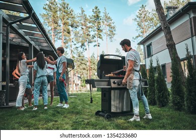 Handsome Man Is Making Grill Barbecue. Group Of Friends Are Having Bbq Party Outdoors On The Backyard.