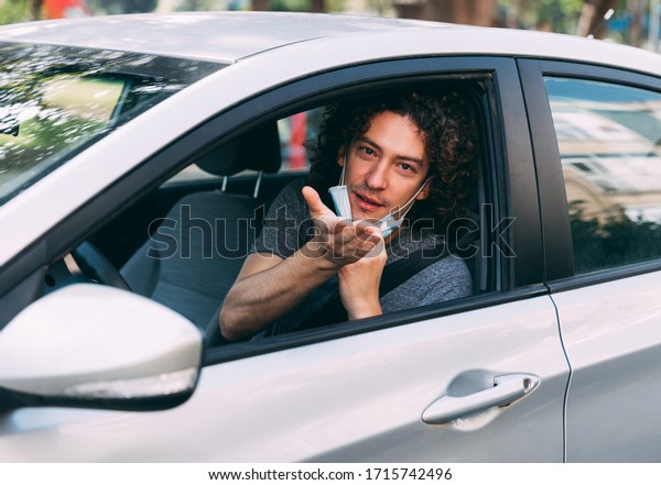 A handsome man with a medical mask driving a car,\
blows a kiss. A man with a protective mask is sitting behind the\
wheel of a car. Protection from coronavirus epidemic pandemic,\
covid-19. New reality