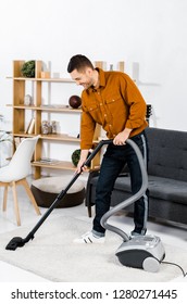 Handsome Man In Modern Living Room Smiling And Cleaning House With Hoover 